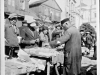Żyd handlujący towarami na rynku głównym w Garwolinie. Na zdjęciu uchwyceni zostali również mieszkańcy Garwolina, którzy robią zakypy u Żyda, W tle kościół z wieżami przewojennymi. Zdjęcie wykonano w latach 30-tych. Ze zbiorów Aliny Janowskiej - aktorki